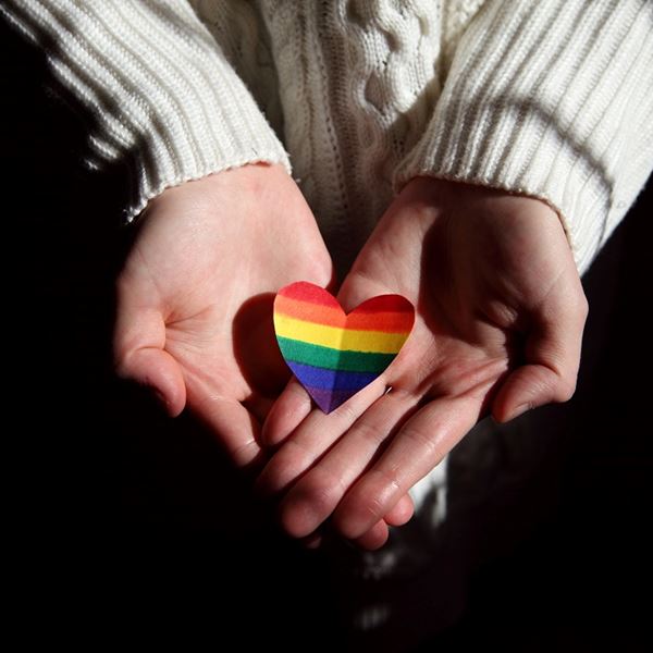 Woman holding heart painted in LGBTQ flag colors.
