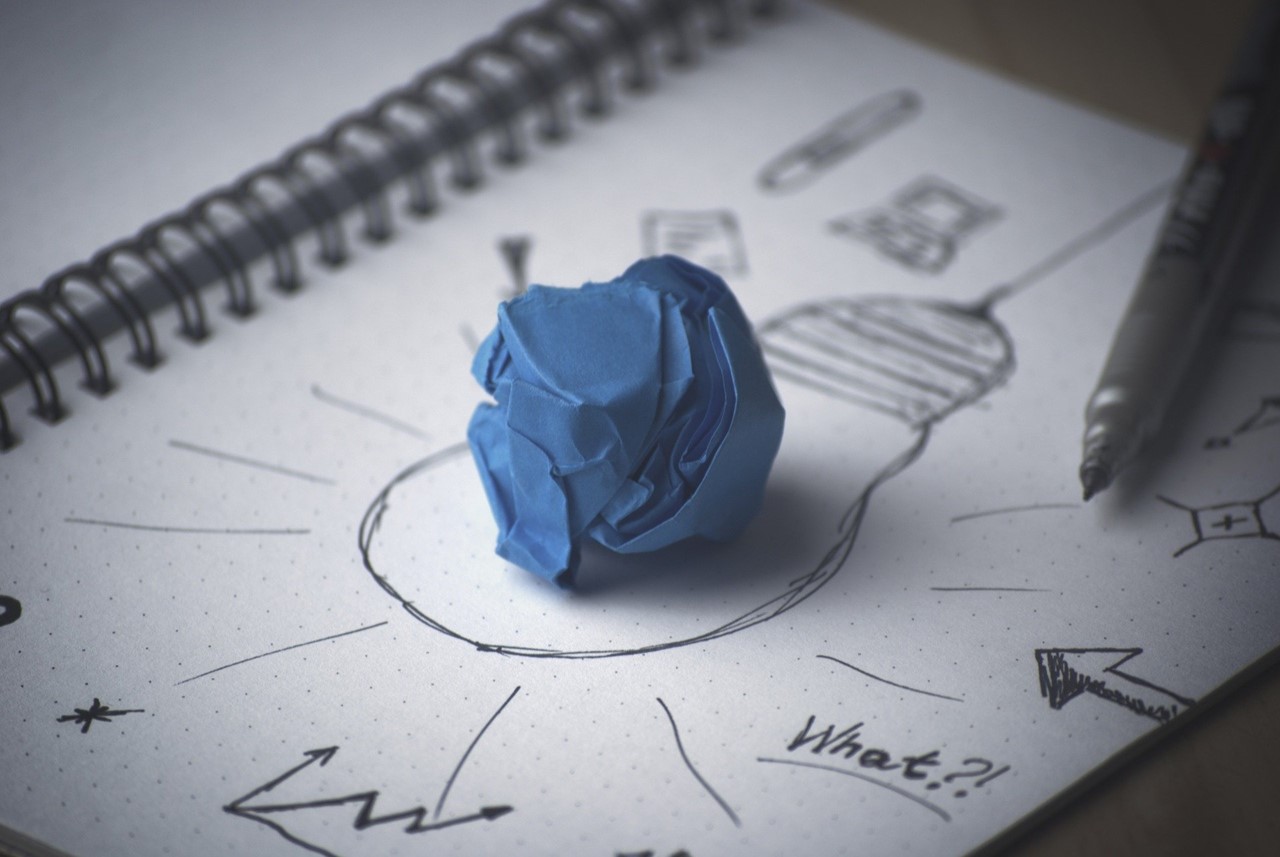 A crumpled paper ball over a book with bulb drawing.